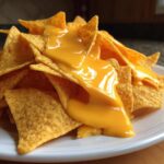 Close-up of crispy tortilla chips smothered in bright, smooth nacho cheese sauce.