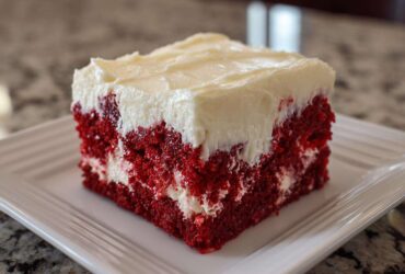 Close-up of a square slice of vibrant red velvet poke cake topped with thick white cream cheese frosting.