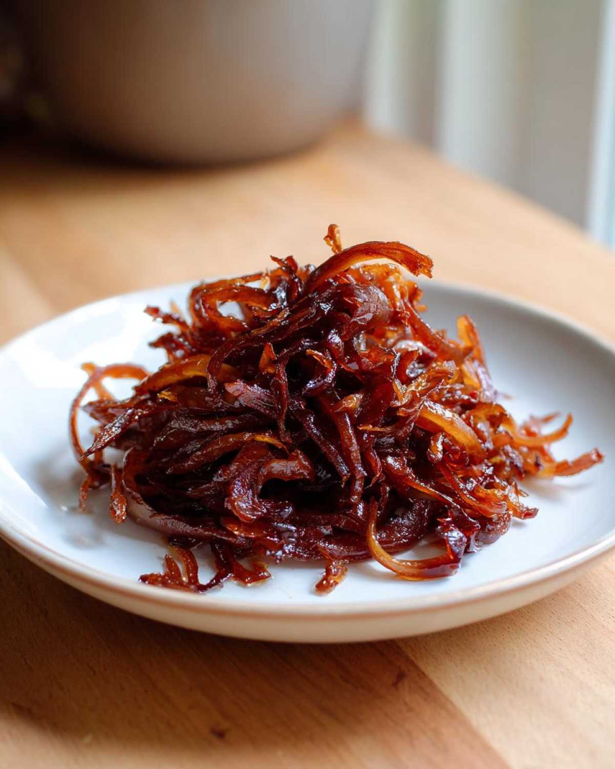 A mound of deeply browned, glossy caramelized onions served on a small white plate.