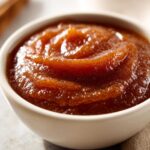 Close-up of thick, dark amber pear butter swirled in a small white bowl.