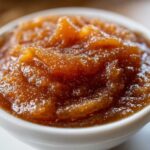 Close-up of rich, dark brown pear butter with a thick, slightly chunky texture served in a small white bowl.