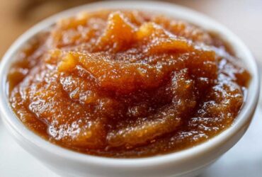 Close-up of rich, dark brown pear butter with a thick, slightly chunky texture served in a small white bowl.