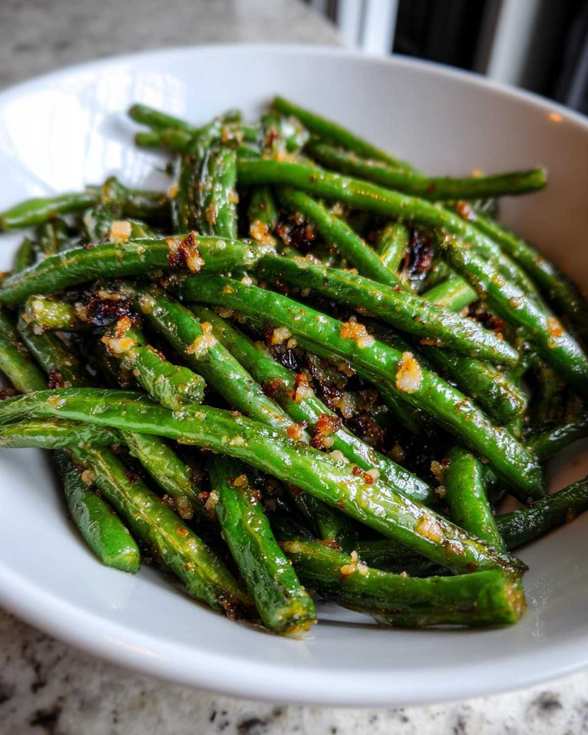A white bowl filled with roasted, glossy green beans seasoned with visible garlic bits.