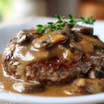 Close-up of a perfectly cooked salisbury steak smothered in rich mushroom gravy and garnished with fresh thyme.