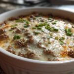 Close-up of a hot, baked sausage cream cheese dip topped with melted cheese and fresh green chives.