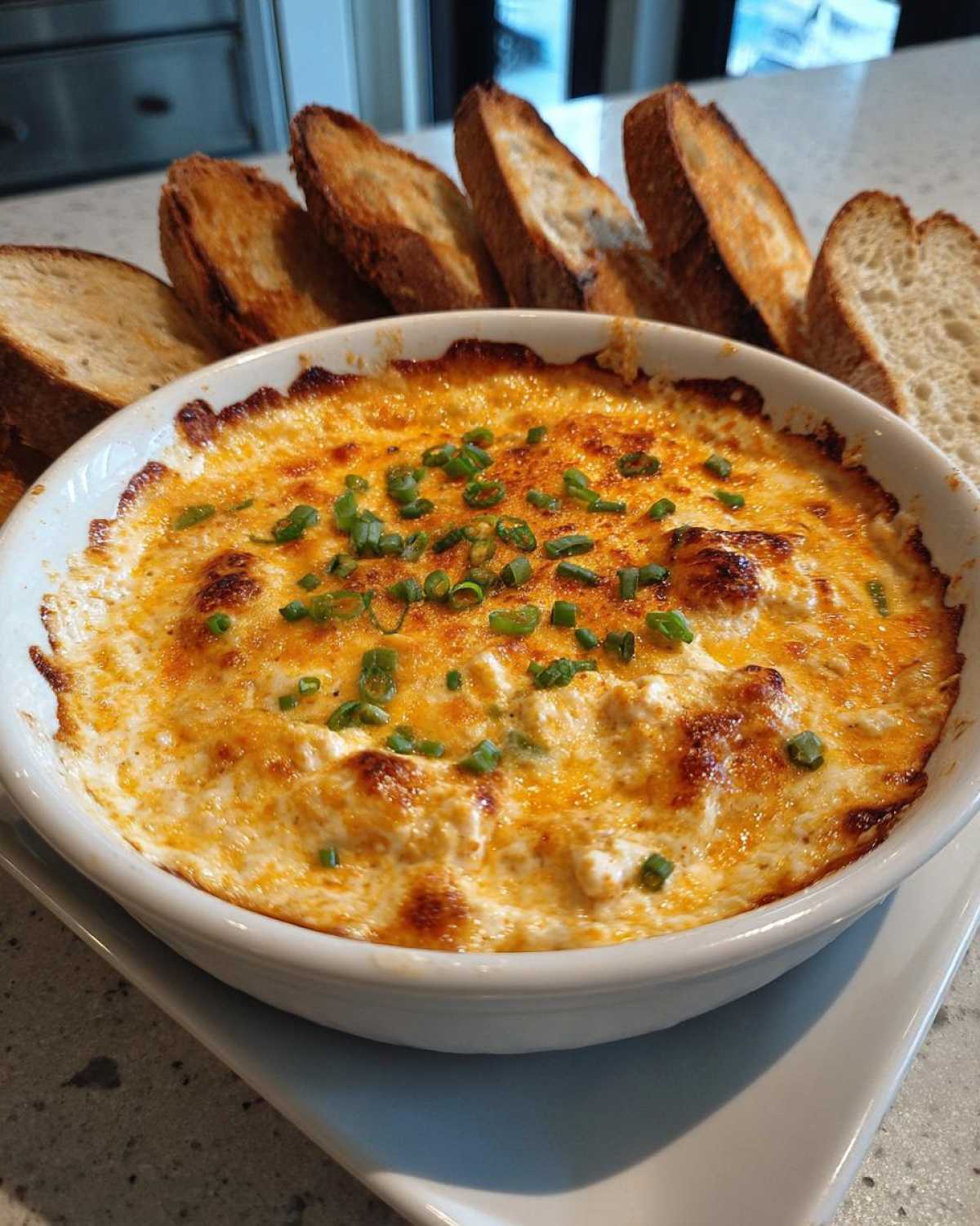 A baked, bubbly sausage cream cheese dip topped with chives, served with toasted baguette slices.
