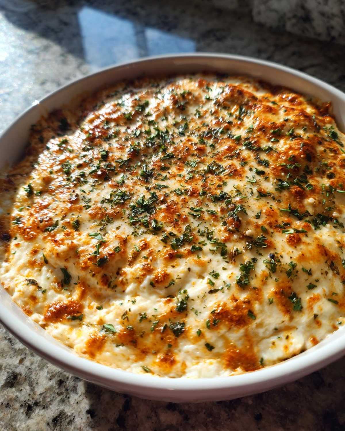 A close-up of a baked sausage cream cheese dip, golden brown and bubbly, topped with chopped parsley.
