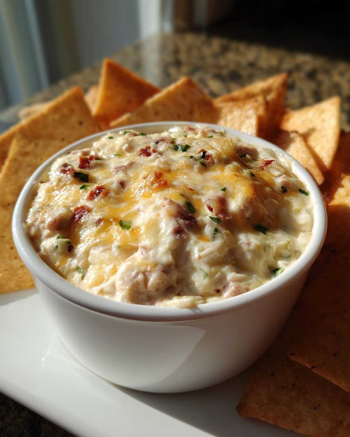 A close-up of hot sausage cream cheese dip topped with melted cheese and chives, served with tortilla chips.