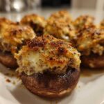 A close-up of several golden-brown, baked sausage stuffed mushrooms with a cheesy, herbed topping.