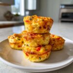 A stack of three golden-brown Egg Muffin Cups filled with visible red and green peppers on a white plate.