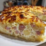 A thick slice of scalloped potatoes and ham bake with a bubbly, browned cheese crust, served on a white plate.