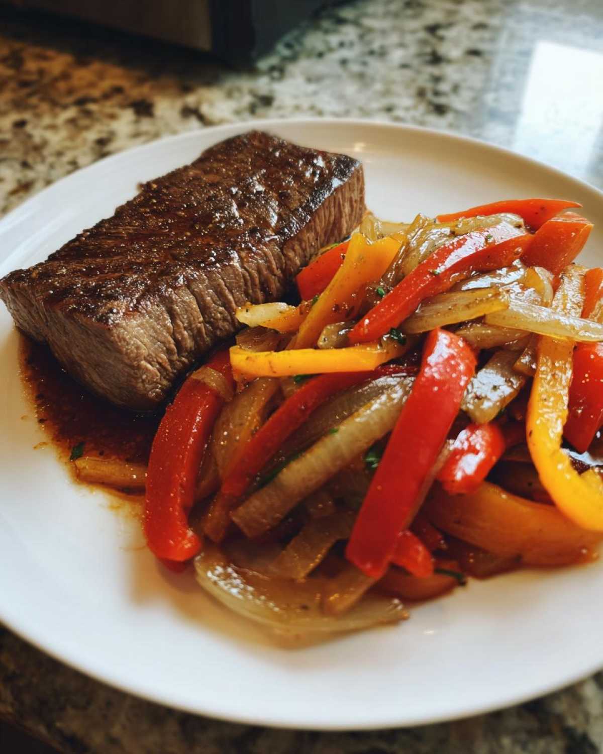 A perfectly seared piece of steak served next to sautéed bell peppers and onions, a key component of steak fajitas.