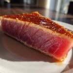 Close-up of a perfectly seared tuna steak, showing a dark crust and bright red raw center, prepared with a MARINADE FOR TUNA STEAK.