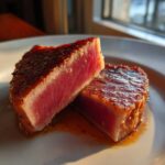 Two pieces of seared tuna steak, cut to show the rare, pink center, coated in a flavorful MARINADE FOR TUNA STEAK.