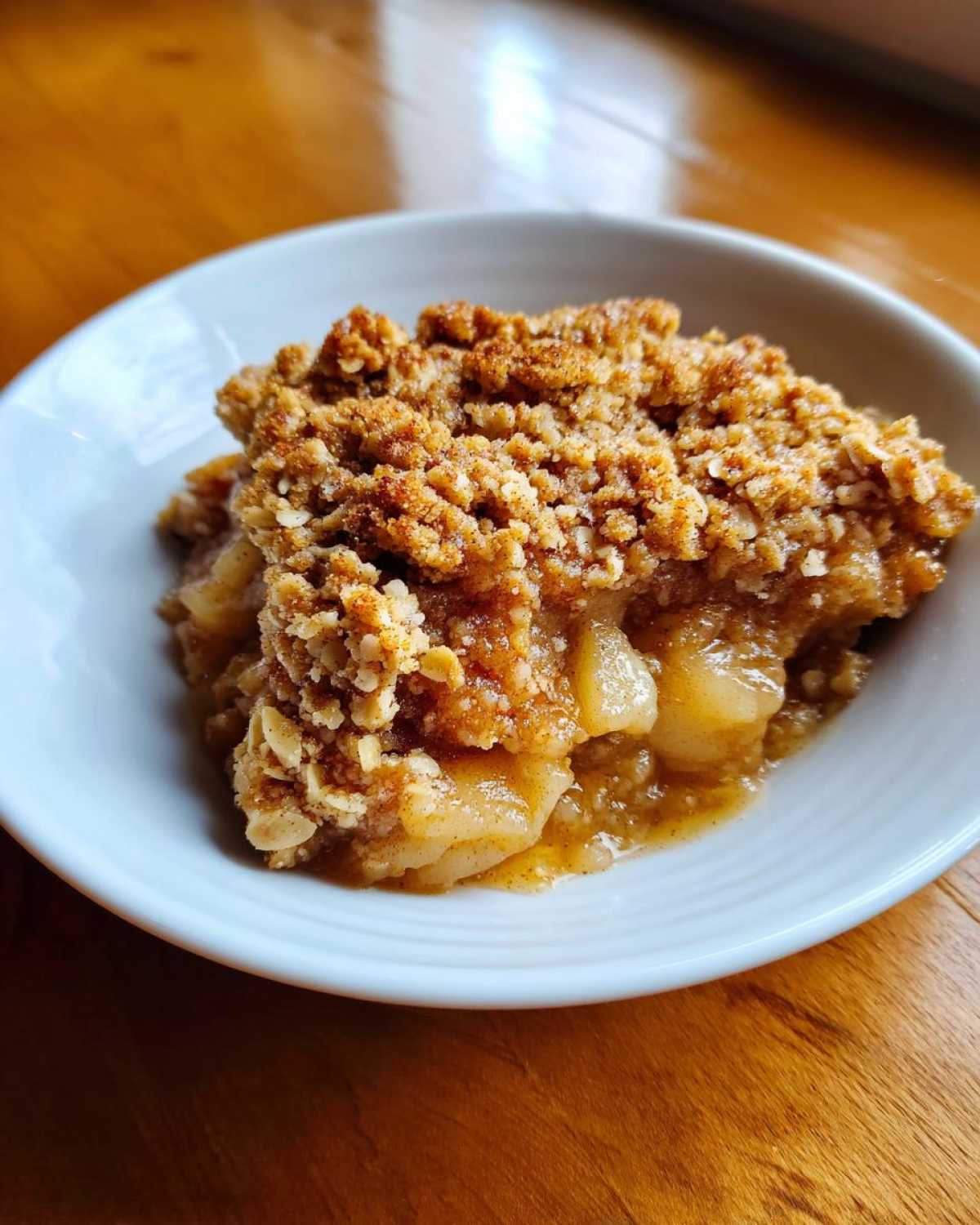 Close-up of a warm serving of amazing 5-star pear crisp with a thick, golden oat topping in a white bowl.