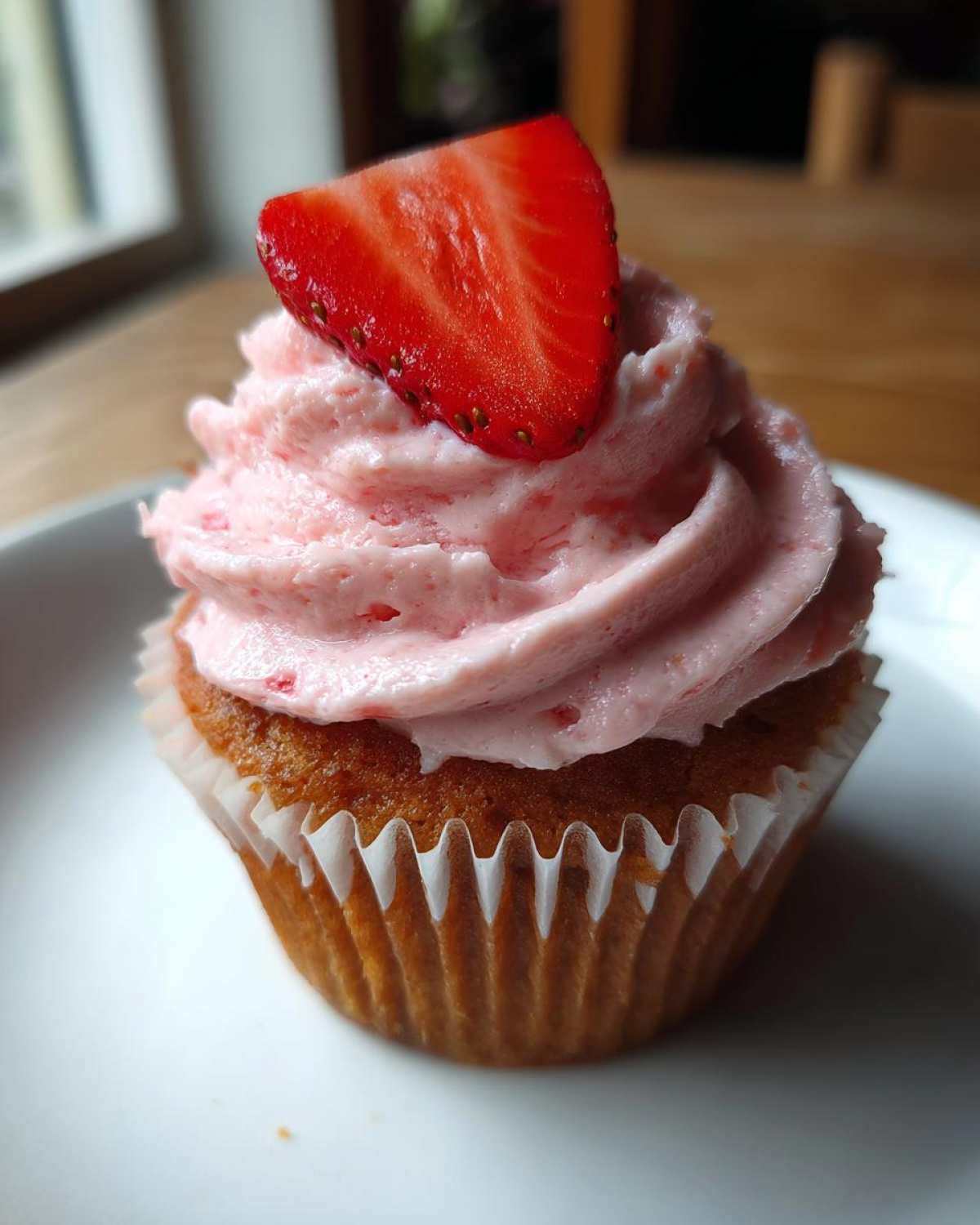 A single, perfectly baked strawberry cupcake topped with pink strawberry frosting and a fresh strawberry slice.
