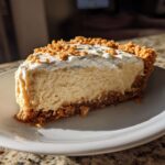 A close-up slice of creamy peanut butter pie with a graham cracker crust and whipped topping sprinkled with crumbs.