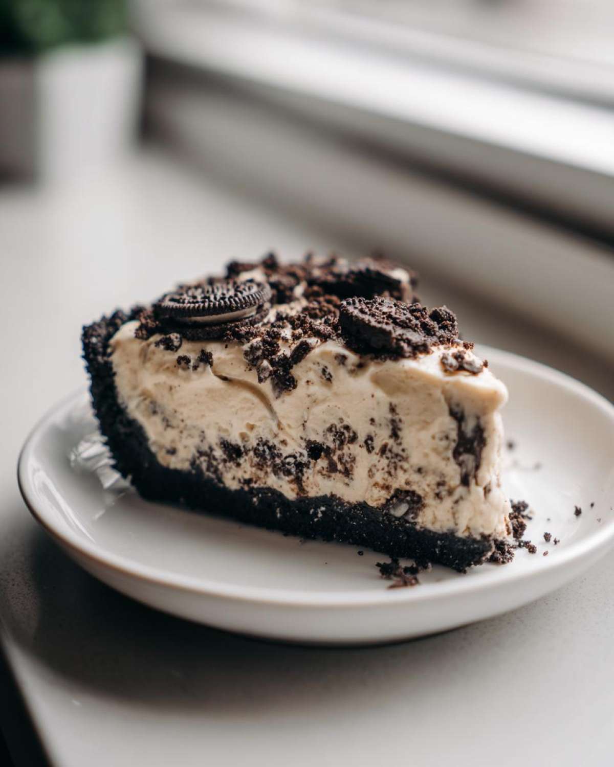 A close-up of a single slice of creamy ice cream pie with a dark chocolate crust and cookie crumbles.