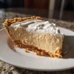 A thick slice of creamy peanut butter pie with a graham cracker crust and whipped topping.