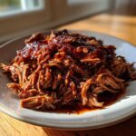 A generous serving of saucy, shredded Slow Cooker Pulled Pork piled high on a light-colored plate.