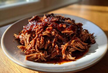 A generous serving of saucy, shredded Slow Cooker Pulled Pork piled high on a light-colored plate.