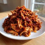 A generous mound of tender, saucy Slow Cooker Pulled Pork piled high on a white plate.