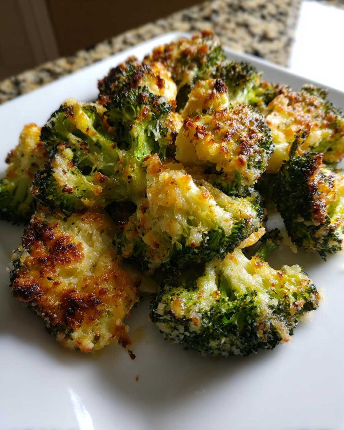 A close-up of crispy, oven-roasted smashed broccoli florets topped with golden, browned cheese.