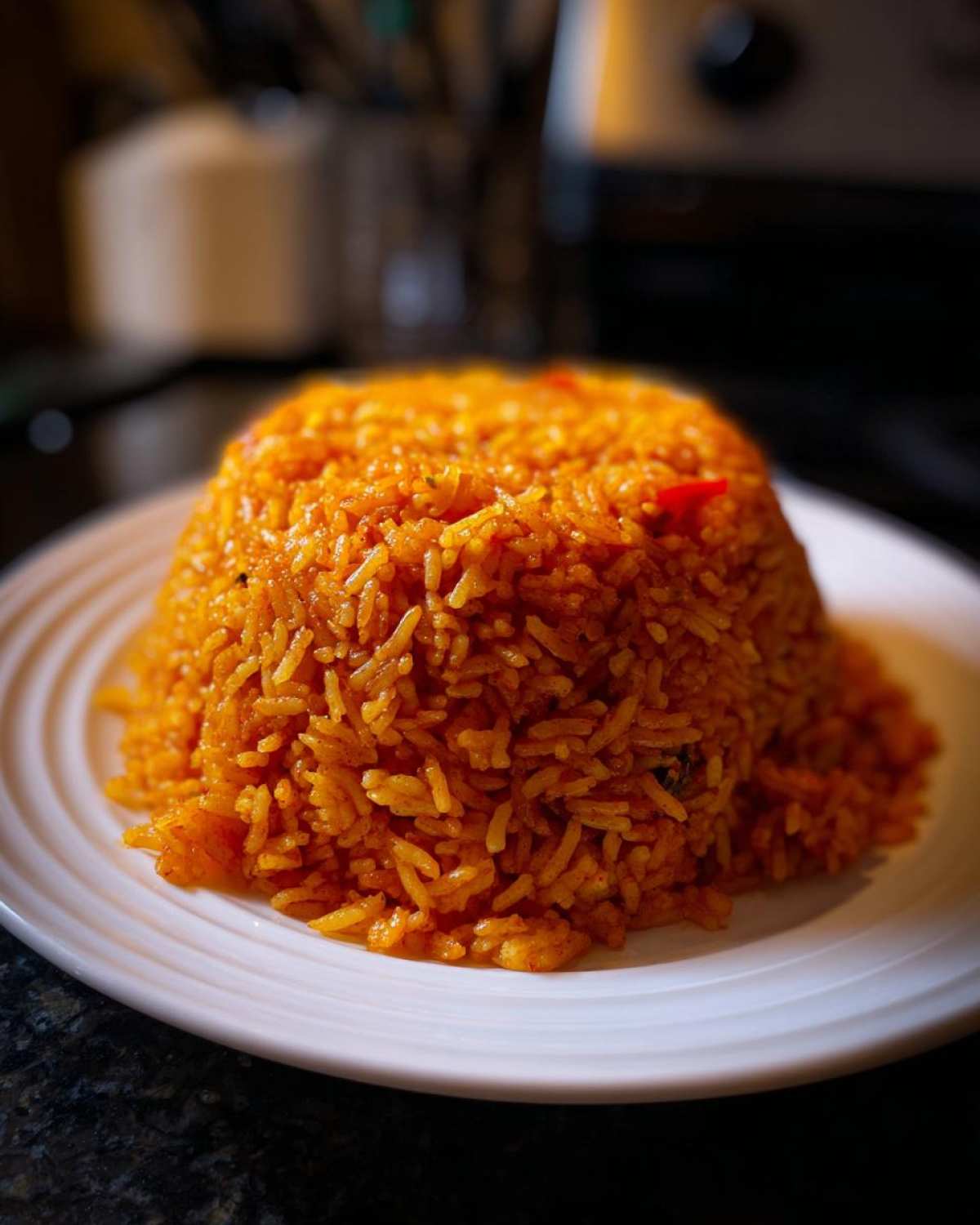 A perfectly molded mound of vibrant, smoky Nigerian jollof rice served on a white plate.