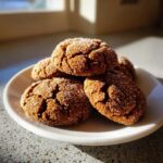 A stack of four soft and chewy ginger molasses cookies coated in sparkling sugar, sitting on a white plate.