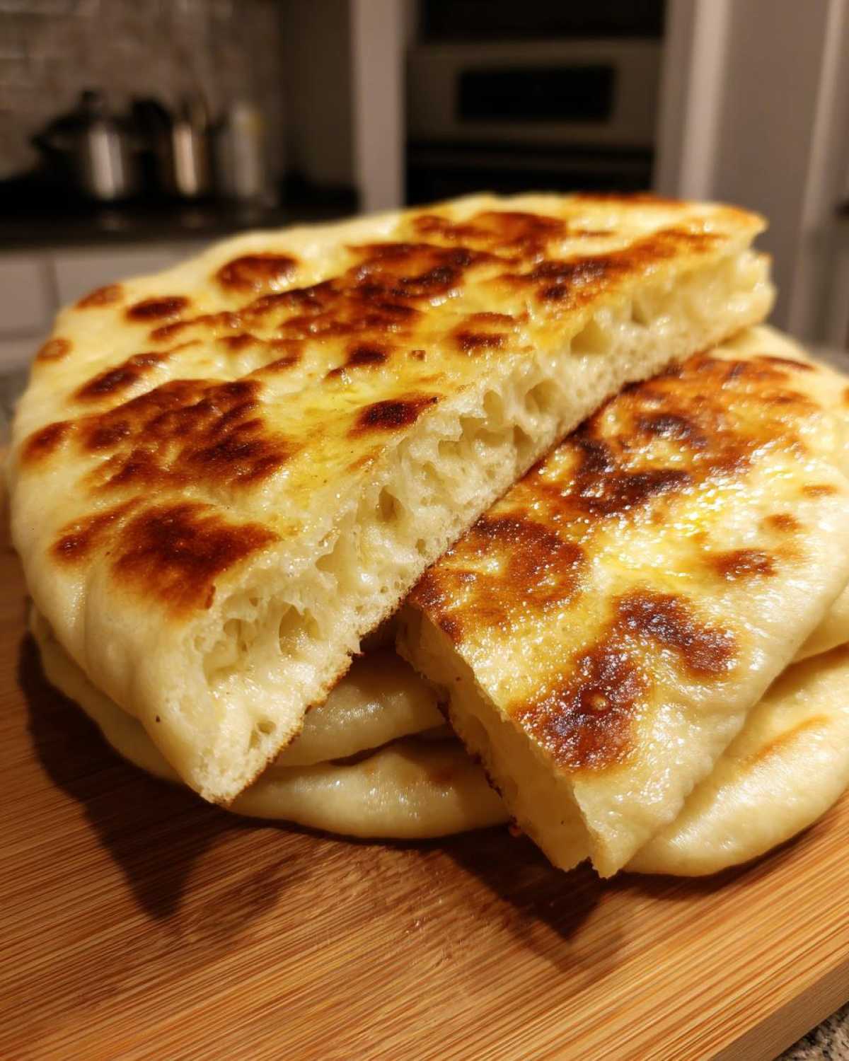 Close-up of soft, fluffy naan bread recipe stacked on a wooden board, showing the airy interior.