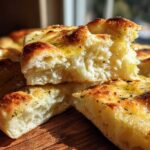 A close-up cross-section showing the fluffy, airy interior of freshly baked naan bread, drizzled with oil and herbs.