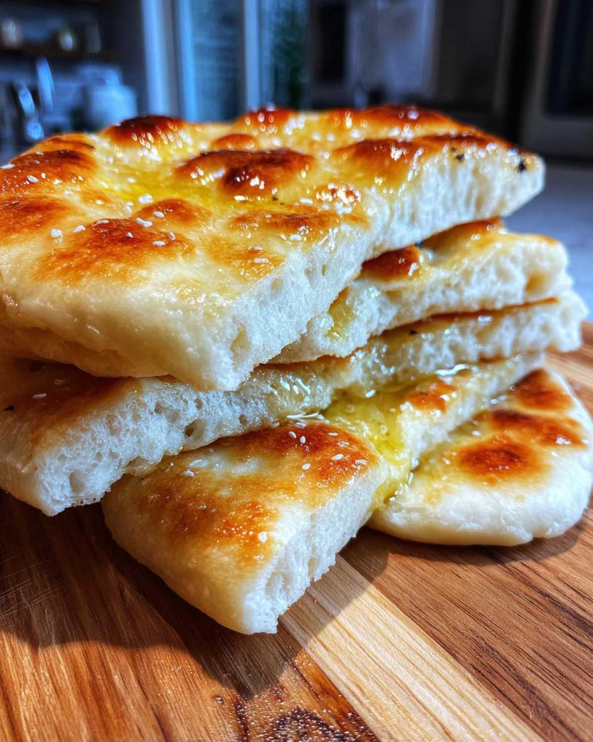 Close-up of stacked, fluffy naan bread recipe pieces brushed with melted butter and sprinkled with sesame seeds.
