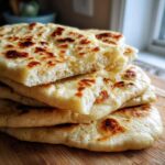 Close-up of a stack of freshly made, soft naan bread recipe pieces with golden-brown charred spots.