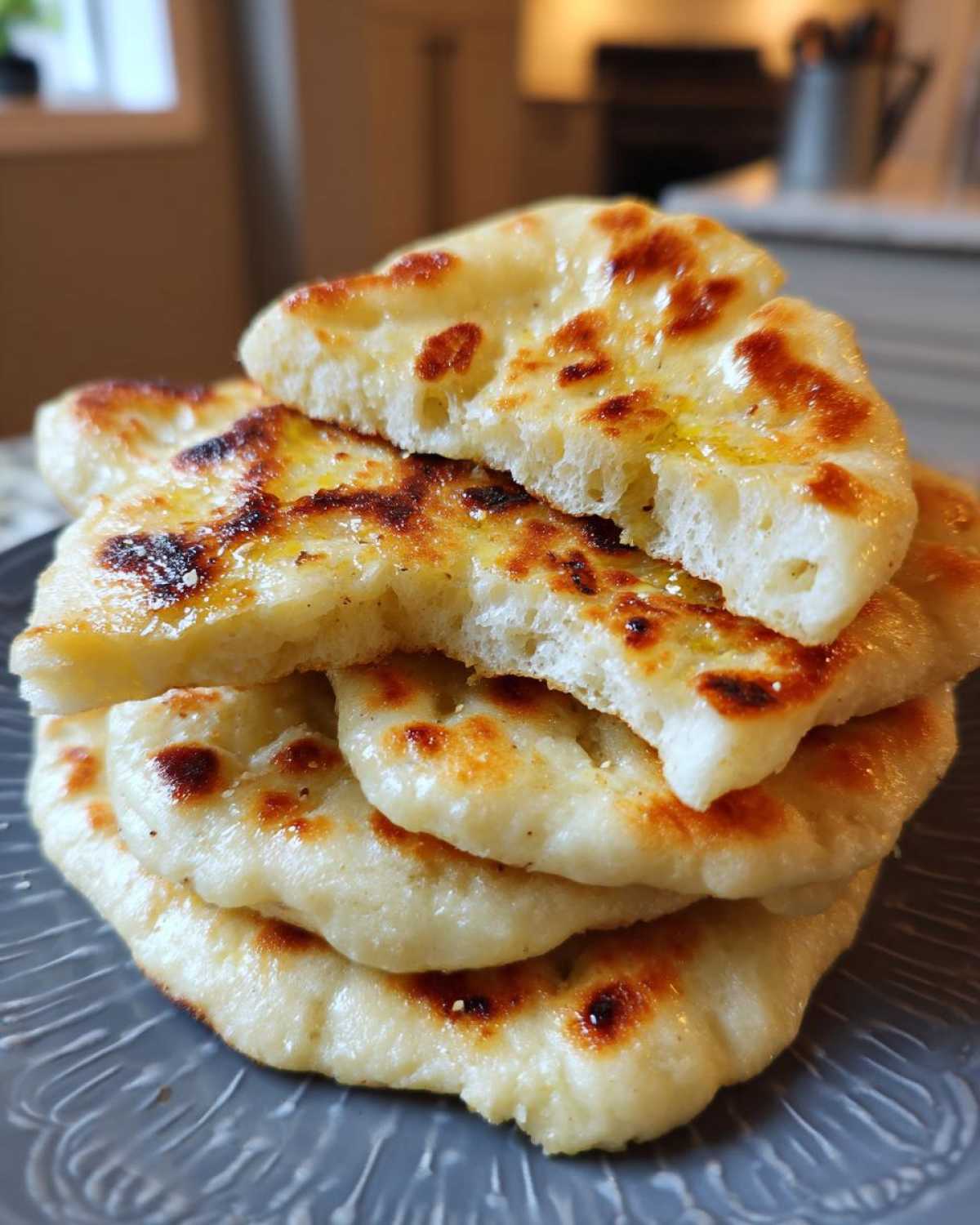 A stack of four soft, slightly charred homemade naan bread recipe pieces, drizzled with butter.