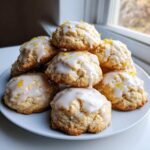 A stack of soft ricotta cookies drizzled with white lemon glaze and topped with bright yellow lemon zest.
