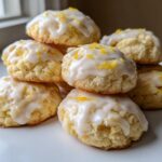 A stack of soft ricotta cookies topped with white glaze and bright yellow lemon zest.