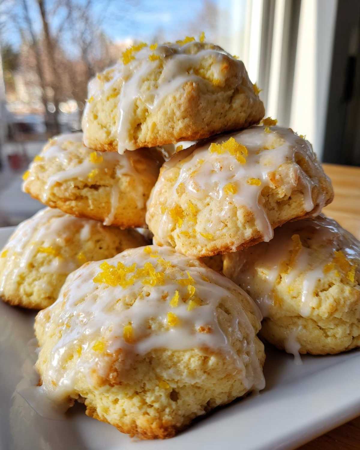 A stack of soft ricotta cookies drizzled with white glaze and topped with bright yellow lemon zest.