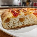 Close-up of a slice showing the airy, open crumb structure of sourdough discard pizza dough with tomato sauce.