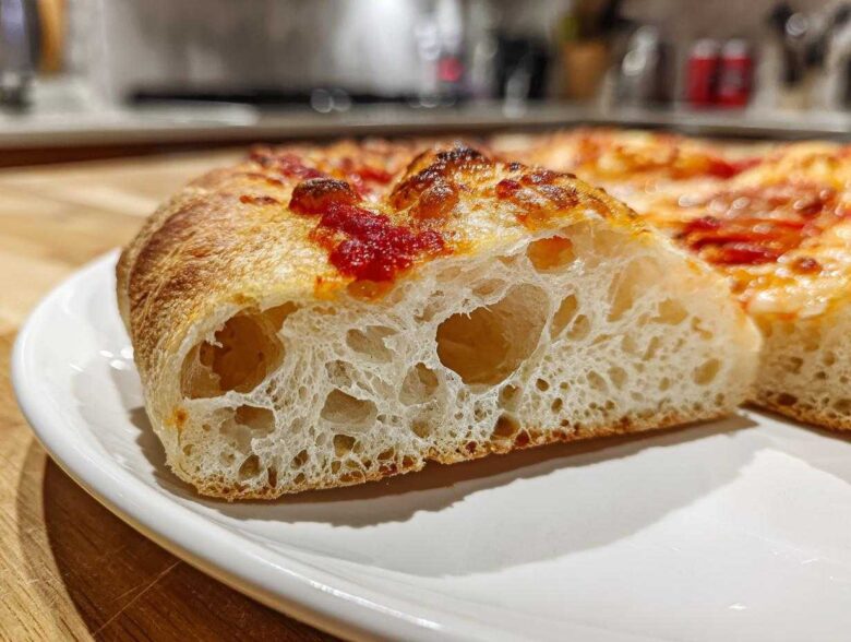 Close-up of a slice showing the airy, open crumb structure of sourdough discard pizza dough with tomato sauce.