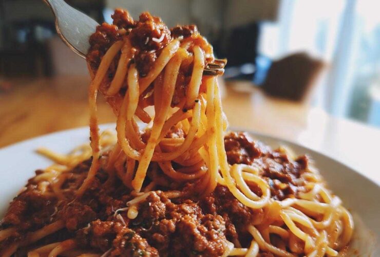 A fork lifting spaghetti noodles coated in rich, meaty bolognese sauce from a white plate.