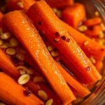 Close-up of bright orange pickled carrots sticks submerged in brine with visible chili flakes and garlic cloves.