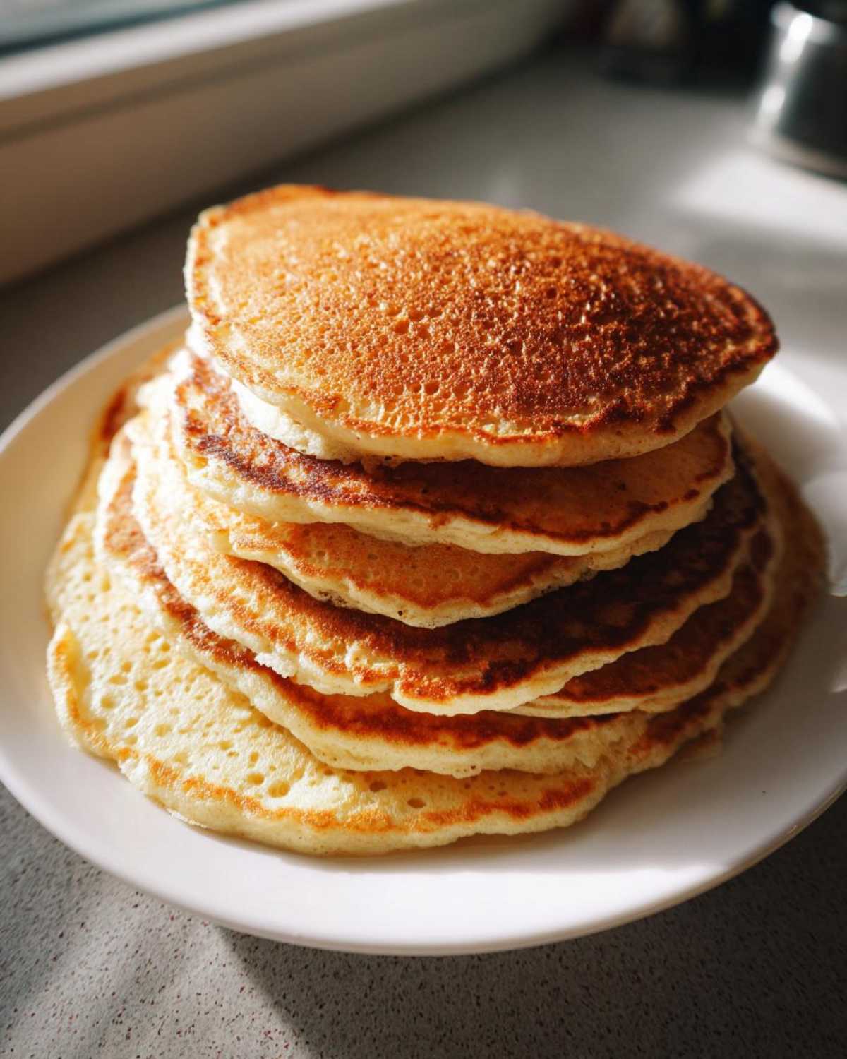 A tall stack of golden brown almond flour pancakes served on a white plate in natural sunlight.