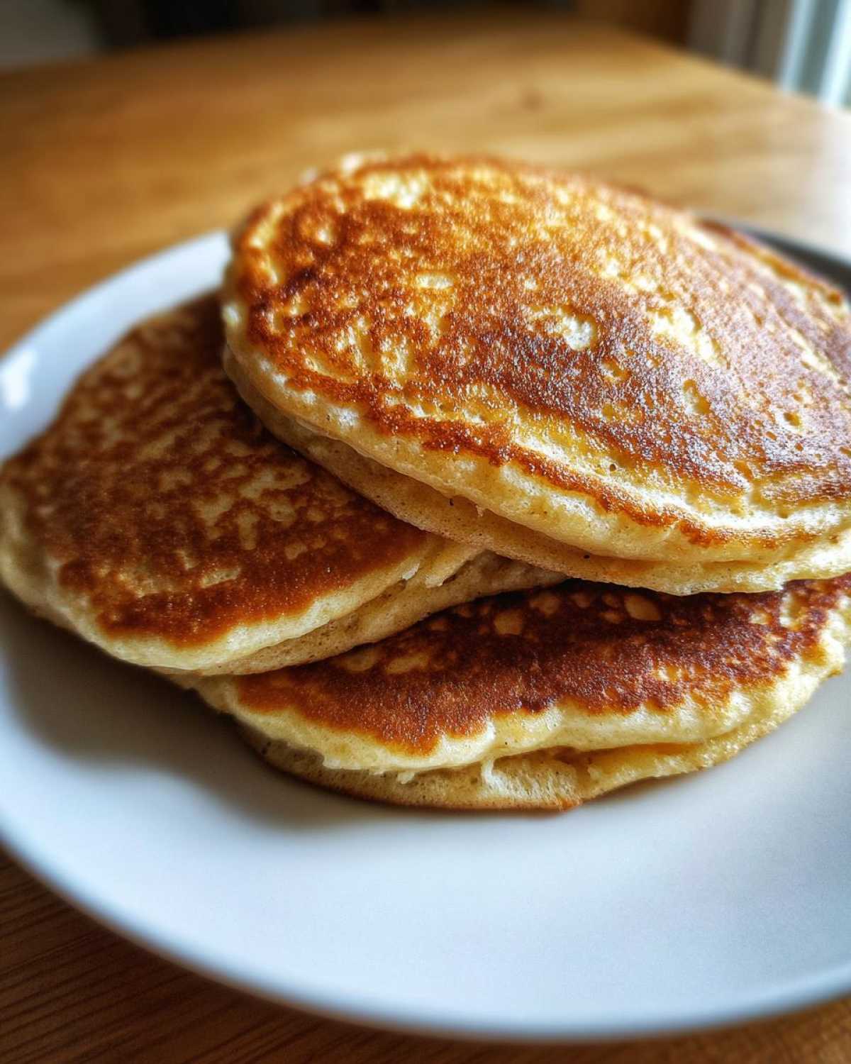 A close-up stack of three fluffy, golden-brown almond flour pancakes resting on a white plate.
