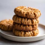 A close-up stack of four perfectly baked peanut butter cookies with classic fork crosshatch marks.