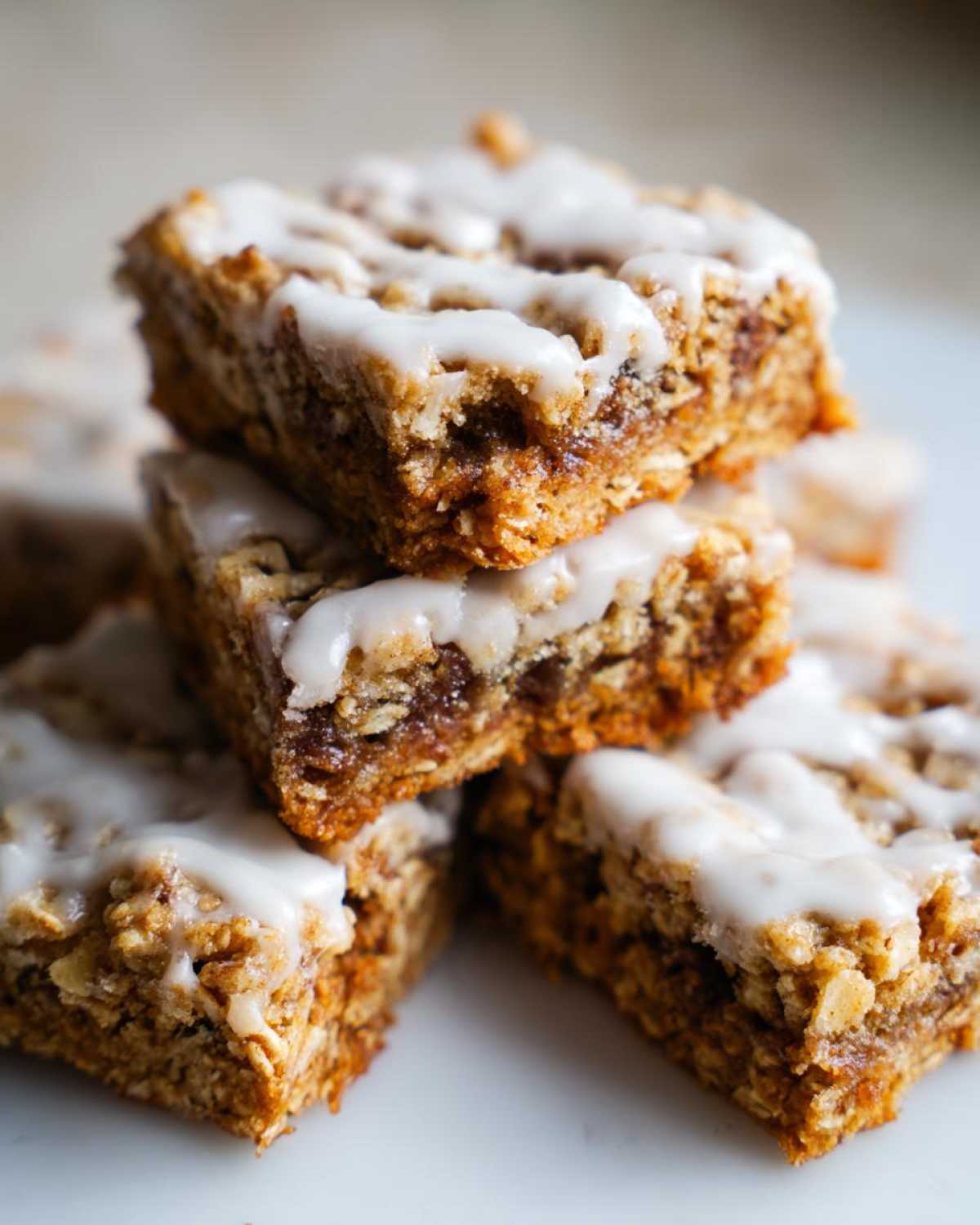 A stack of delicious, square oatmeal bars topped with a thick white glaze or icing.