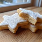 A stack of star-shaped vegan sugar cookies topped with white icing and fine sprinkles.