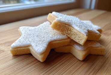 A stack of star-shaped vegan sugar cookies topped with white icing and fine sprinkles.
