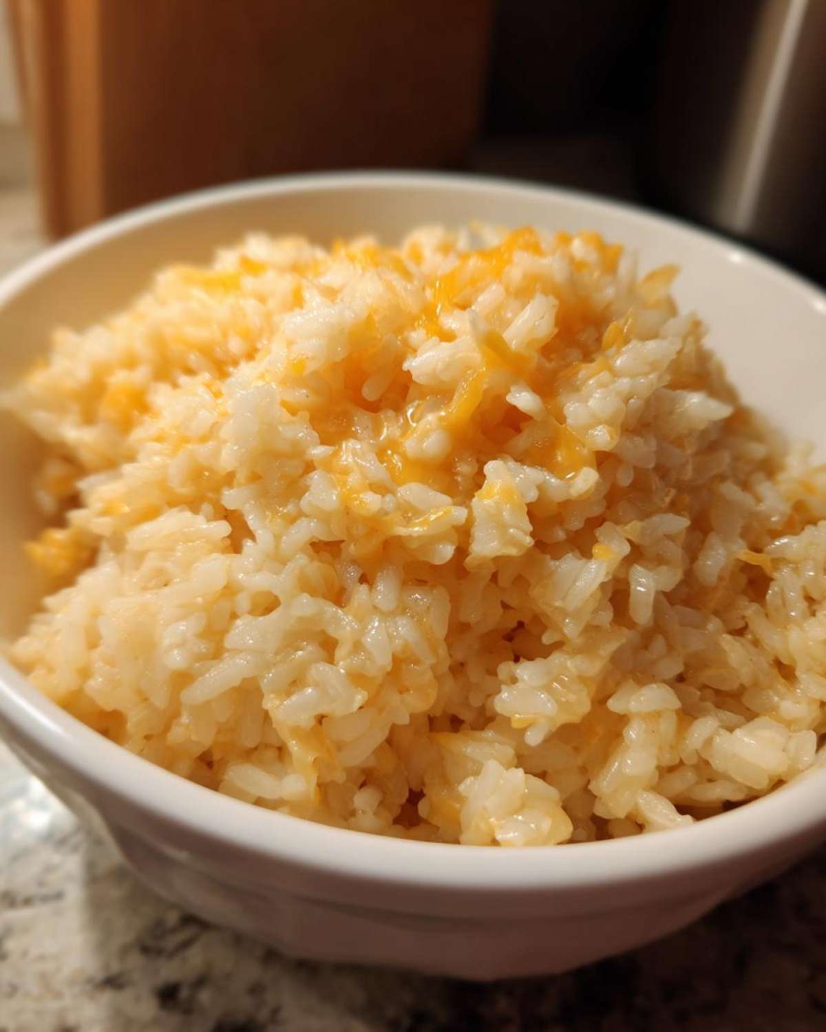 Close-up of fluffy white rice mixed with melted shredded cheddar cheese, served in a white bowl, showcasing the cheesy rice.