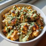 Close-up of a street corn chicken rice bowl topped with cotija cheese, cilantro, and a creamy green sauce.