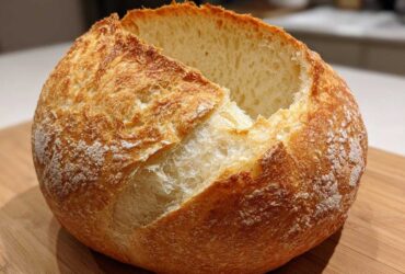 A golden-brown, round loaf of artisan bread with a scored top, ready to be turned into sturdy bread bowls.